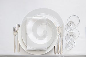 White table setting from above. Elegant empty plate, cutlery, napkin and glass