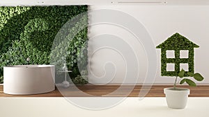 White table top or shelf with green plant in pot shaped like house, minimal bathroom with vertical garden in the background,