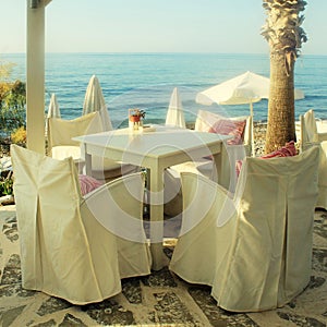 White tables and chairs in greek cafe by the sea coast, Crete, G