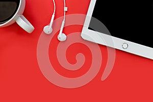 White tablet computer earphones and coffee cup on bright red background