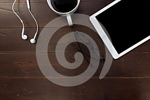 White tablet computer earphones and coffee cup on dark brown tab