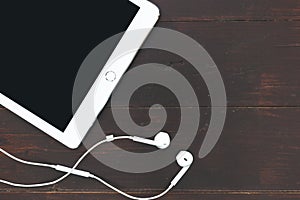 White tablet computer music earphones on dark brown table background