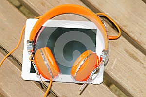 White tablet PC with orange headphones on the wood bench
