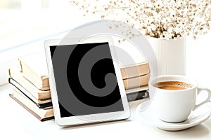 White tablet sits on a table next to a cup of coffee and a stack of books.