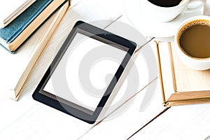 White tablet sits on a table next to a cup of coffee and a stack of books.