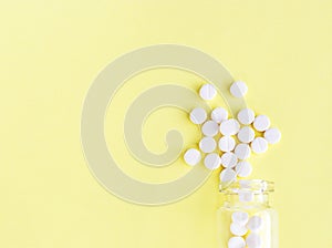 White tablets from a glass bottle on a yellow background. Health care, painkillers and medicinal pills
