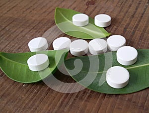 White tablets and green leaves over wooden background symbolizing homeopathy.