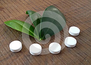 White tablets and green leaves over wooden background symbolizing homeopathy.