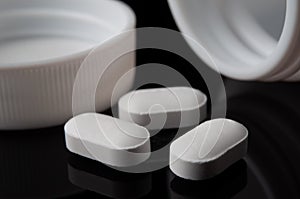 White tablets of medicine pouring out of the pill bottle on black background