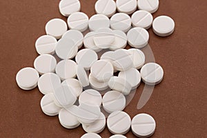 White tablets are scattered from a bottle on a brown background