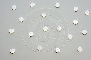 White tablets scattered on gray background form a speckled ornament. Photo for use in medicine, pharmacy, pharmaceutical productio