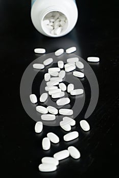 White tablets spilled from a bottle on a dark surface in a studio