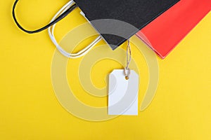 White tag with paper red and black recyclable bag on yellow background. Paper bag handles