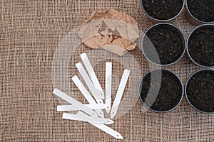 White tags and brown pots with soil on sackcloth background.