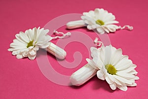 White tampons and flowers on a pink background