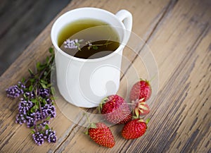 White tea Cup with grass thyme and strawberries on a wooden background top view