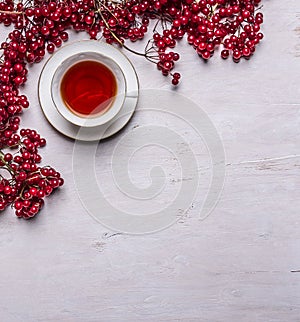 White tea cup on a saucer Bunches of berries Viburnum on rustic wooden background top view space for text