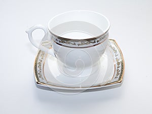 White tea mug with golden border stands on a saucer on a white background