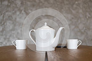 white tea set teapot and two cups stand on a brown table