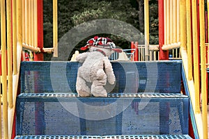 The white teddy bear in the red hat is understood by the blue stairs to the slide on the playground.