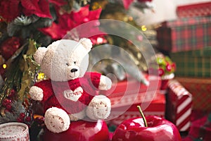 White Teddy bear in red knitted sweater with heart on the chest and the words Love near Christmas tree among the gift boxes. Gift