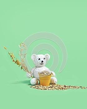 A white teddy bear sits and holds ears of oats in his hand,