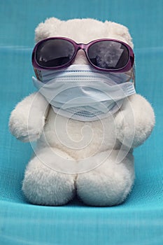 A white teddy bear with sunglasses and a medical mask
