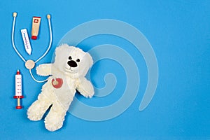 White teddy bear with toy stethoscope and toy medicine tools on a light blue background. Top view. Copy space for text