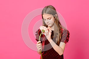 White teen girl with long hair in a red dress with a flower on a pink background