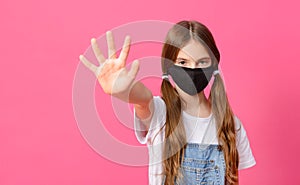 White teenage girl in a black mask on a pink background shows her hand stop