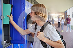 White teenage schoolboy using locker in school corridor