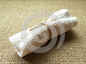 White terry towel rolled on linen burlap sacking background. Spa, sauna, healthy lifestyle concept