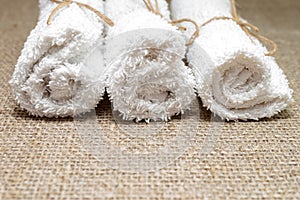 White terry towel rolled on linen burlap sacking background. Spa, sauna, healthy lifestyle concept