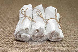 White terry towel rolled on linen burlap sacking background. Spa, sauna, healthy lifestyle concept