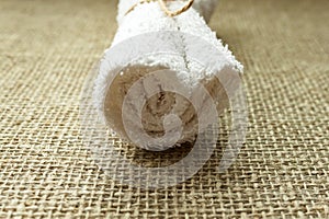 White terry towel rolled on linen burlap sacking background. Spa, sauna, healthy lifestyle concept