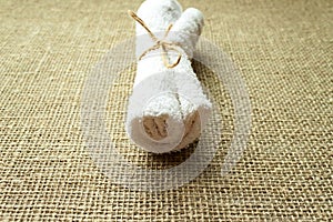 White terry towel rolled on linen burlap sacking background. Spa, sauna, healthy lifestyle concept