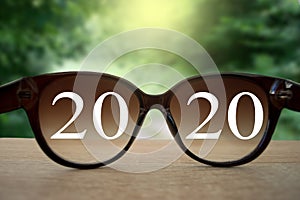 2020 white text with black eye glasses on wooden table over blur autumn landscapes. Business vision happy new year..