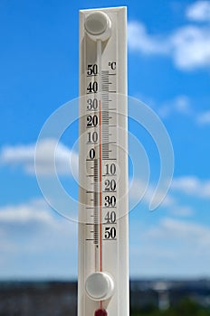 White thermometer against blue sky shows high temperature