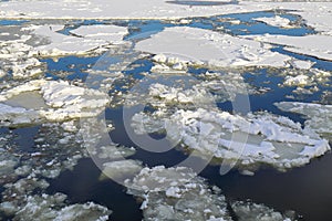 White thick ice floes covered with snow float on a blue river