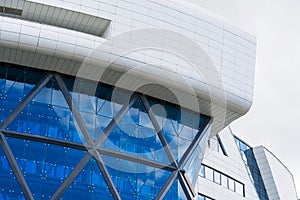 White tiled clad building with large glass windows reflecting blue sky under daytime sunbeams