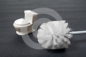 White toilet brush and small toilet bowl on grey background. Tools for house cleaning hygiene