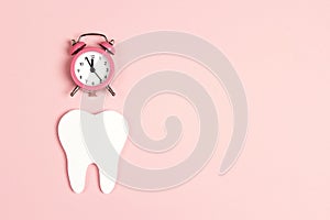 White tooth with alarm clock on pink background. Time to dental health. Dentist day concept