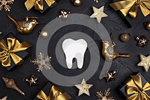 White tooth with golden decorations and gift boxes on black background. Dentist Merry Christmas and New Year concept