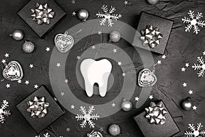 White tooth with silver decorations and gift boxes on black background. Dentist Merry Christmas and New Year concept