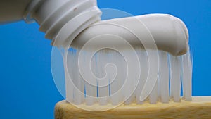 White toothpaste coming out of tube on wooden bamboo brush at blue background