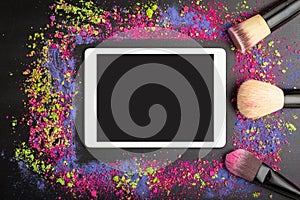 White touchpad with blank touchscreen with professional makeup brushes on colorful background of crumbled eyeshadows