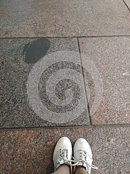 White tourist sneakers are on the brown marble floor. The floor is gray and brown squares. Tourist pending.