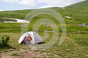 White tourist tent against the backdrop of a campsite among alpine meadows.