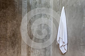 The white towel is hanging on a hanger with concrete wall in the