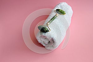 White towel and roller massager and gouache scraper on a pink background. Spa treatments with massagers